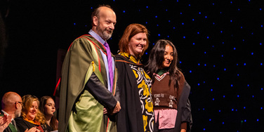 Professor John Craig (Pro Vice Chancellor, University of Hull), Patsy Gilbert (Vice Principal, Leeds Conservatoire) and Lily Fontaine (frontwoman of English Teacher) on stage at Graduation 2025 in New Dock Hall, Royal Armouries