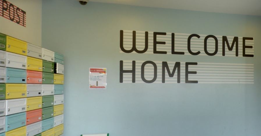 Entrance saying 'Welcome Home' and multi-coloured locked post boxes